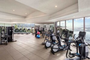 Ein geräumiger Fitnessraum mit Cardiogeräten, Gewichten und Blick auf den Ozean.