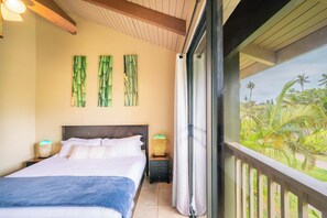 Une chambre d’hôtel avec un lit, deux lampes fixées au mur et une vue sur un jardin tropical.