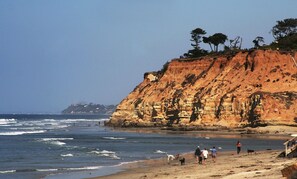 A coastal beach with rocky cliffs and a clear sky.