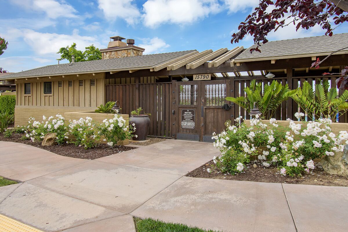 A residential property with a gated entrance, a patio area with potted plants, and a well-maintained garden with white flowering plants.