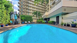 A swimming pool with lounge chairs and potted plants, surrounded by a multi-story building with balconies.