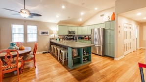 A spacious kitchen with a central island, green cabinets, stainless steel appliances, and a dining area with wooden chairs. - Twelve Palms-Pet Friendly, Golf Cart Zone, Close to Beach, Downtown, City Pool  (Port Aransas)