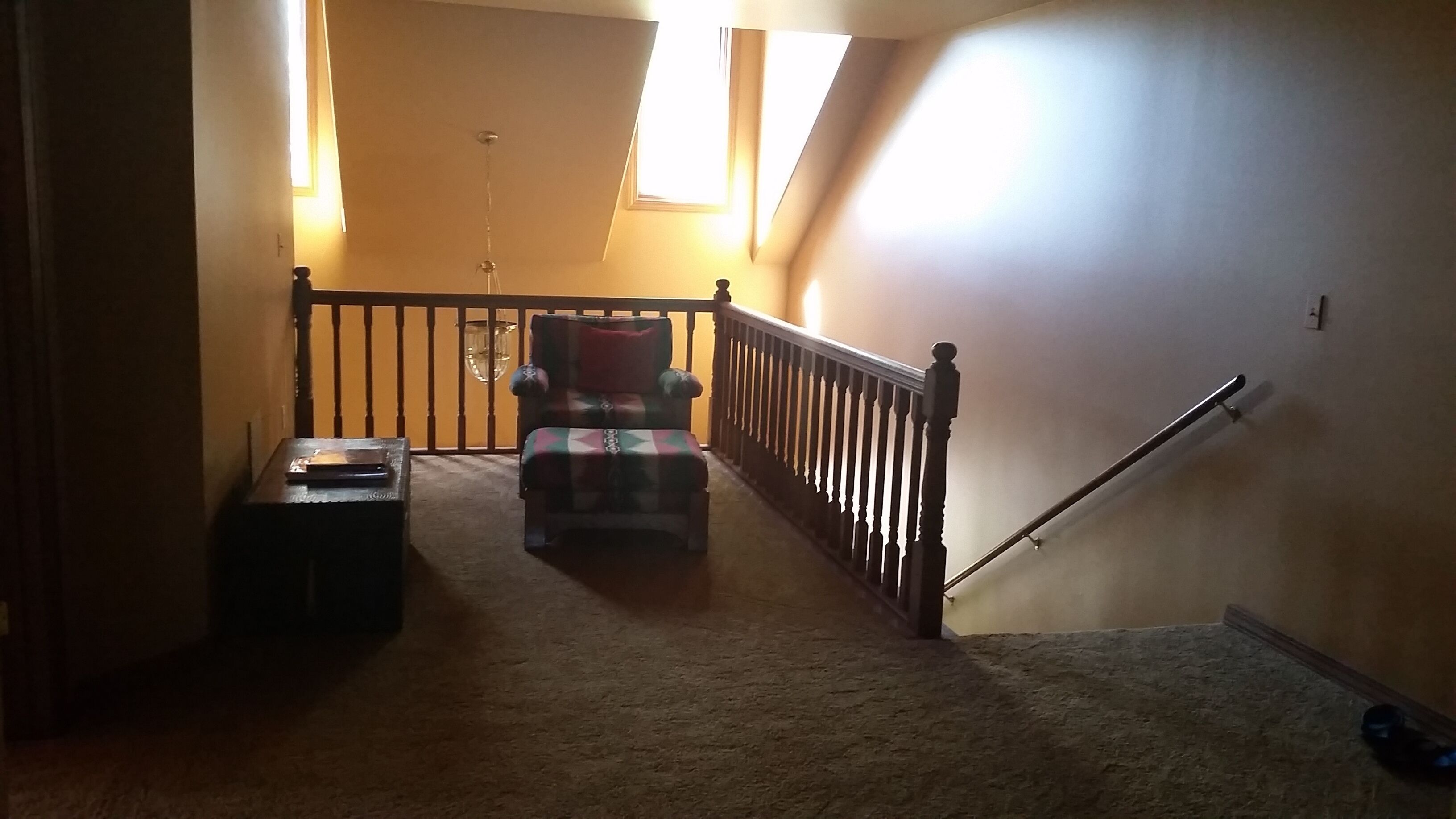 A carpeted hallway with a wooden railing, a chair, and a small table.
