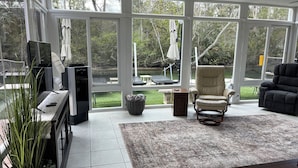 A sunroom with large windows, a fireplace, a television, and a comfortable seating area.