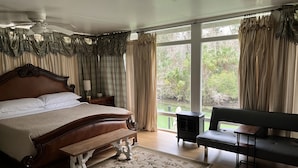 A bedroom with a large bed, a wooden bench, a small table, a nightstand, and a ceiling fan.