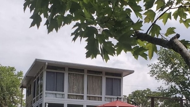 A two-story building with a dock extending into the water, featuring outdoor seating and umbrellas.