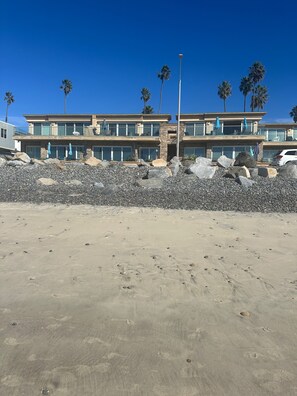Una propiedad frente a la playa con un edificio de dos pisos, costa rocosa y palmeras.