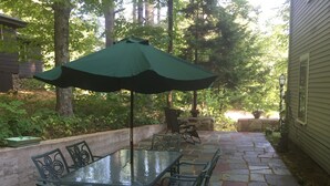 Eine Terrasse im Freien mit einem Glastisch und Metallstühlen, umgeben von Steinplatten und Grünpflanzen.