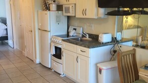 A compact kitchen with white cabinets, a microwave, a toaster, and a small trash bin.