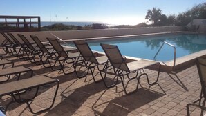 A poolside area with lounge chairs and a clear view of the ocean.