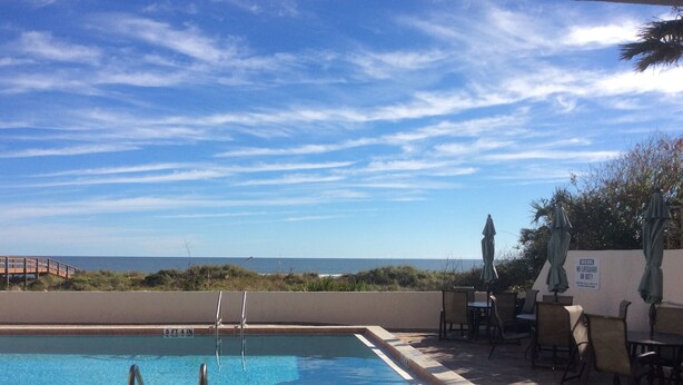 A swimming pool with a view of the ocean, a lifeguard chair, and a warning sign.