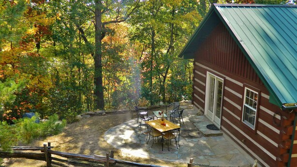 Un chalet rustique doté d’une terrasse en pierre, d’une table en bois et de chaises.