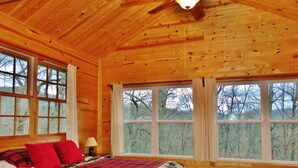 Une chambre dans une cabane en bois, avec un lit, deux fenêtres et un ventilateur de plafond.