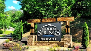 Skiltning for Hidden Springs Resort, med et bjerglogo, omgivet af anlagte haver og en stenvæg.