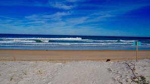 A beach with a clear sky, waves, and a sign in the distance. - AVAIL LABOR DAY WKEND - Steps to Beach - 3BR/3BA - Sleeps 8 - Garage (Palm Coast)