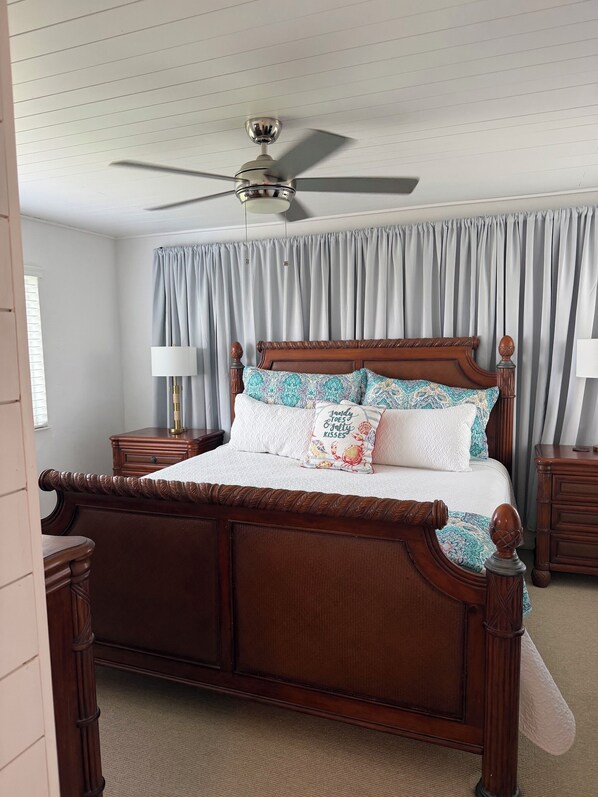 A bedroom with a wooden four-poster bed, a ceiling fan, and a window with curtains.