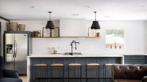 Una cocina moderna con una isla central, taburetes de bar, un refrigerador y una zona de comedor con un sofá de cuero.