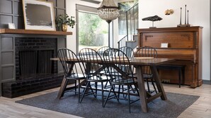 Un comedor con una mesa de madera oscura, sillas negras, una araña, una chimenea y un piano.