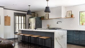 Una cocina moderna con una isla de mármol, taburetes de bar, luces colgantes y vistas al exterior.