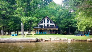 A lakeside cabin with a balcony, surrounded by trees.