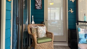 Une véranda aux murs de couleur turquoise, avec un fauteuil en osier, une pancarte de bienvenue et des mouettes décoratives.