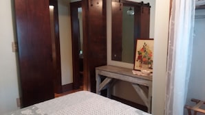 A bedroom with a bed, a wooden wardrobe, a desk with a mirror, and a framed picture on the wall.