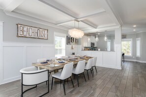 A dining area with a long table, white chairs, and a chandelier.