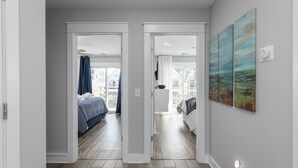 Un pasillo que conduce a un dormitorio con cama, ventana con cortinas y un cuadro en la pared.