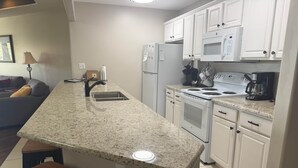 A kitchen with granite countertops, white cabinets, a stove, microwave, and a refrigerator. There are two wooden stools and a coffee maker on the counter. - Emerald Bay Condos Lake Ozark MO (Lake Ozark)
