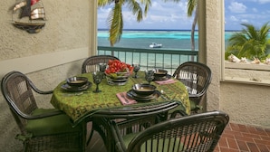Un coin repas avec une table dressée pour deux personnes, donnant sur une mer turquoise et des palmiers.