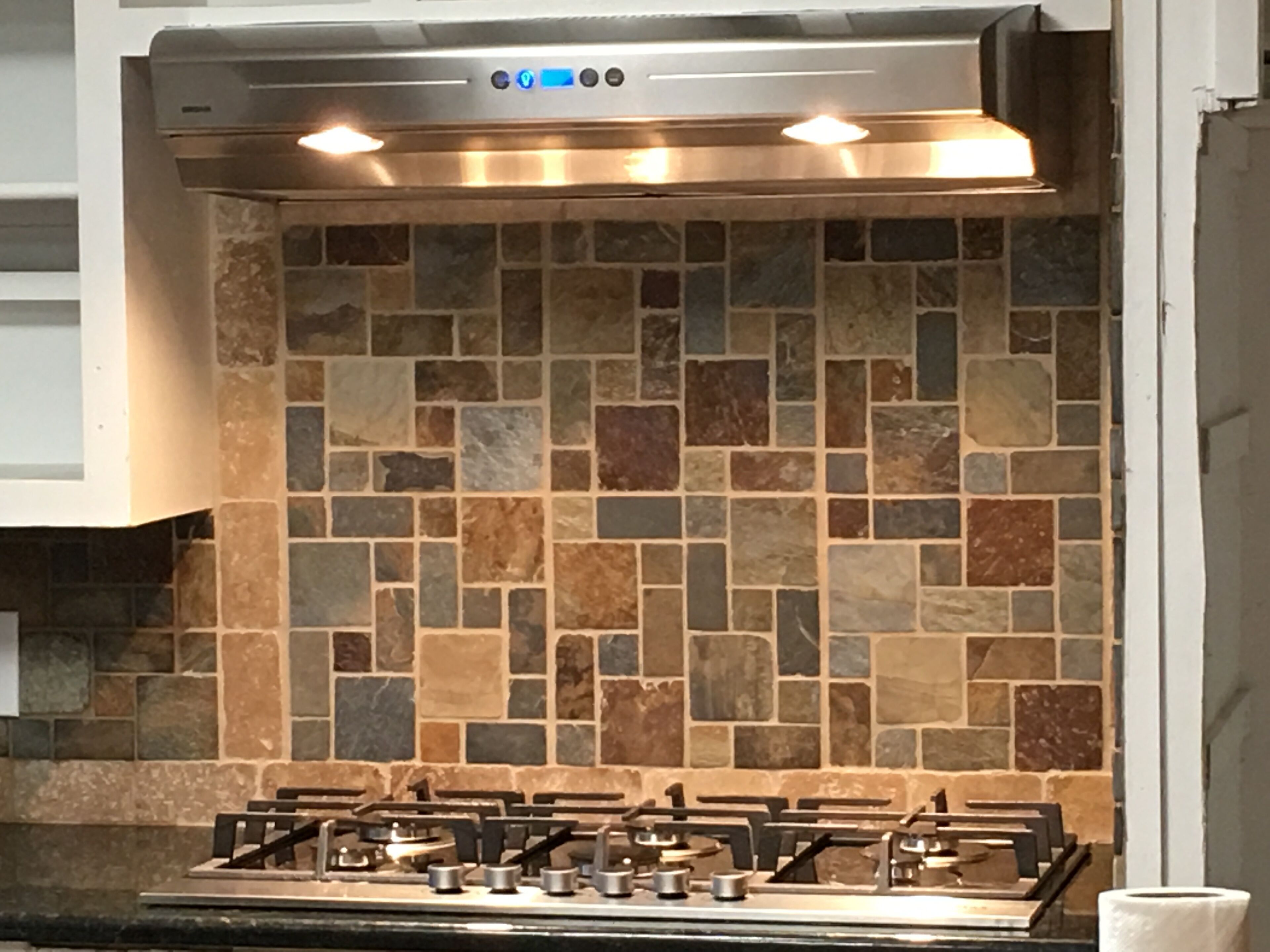 A kitchen with a gas stove, a backsplash of multicolored tiles, and a stainless steel range hood.