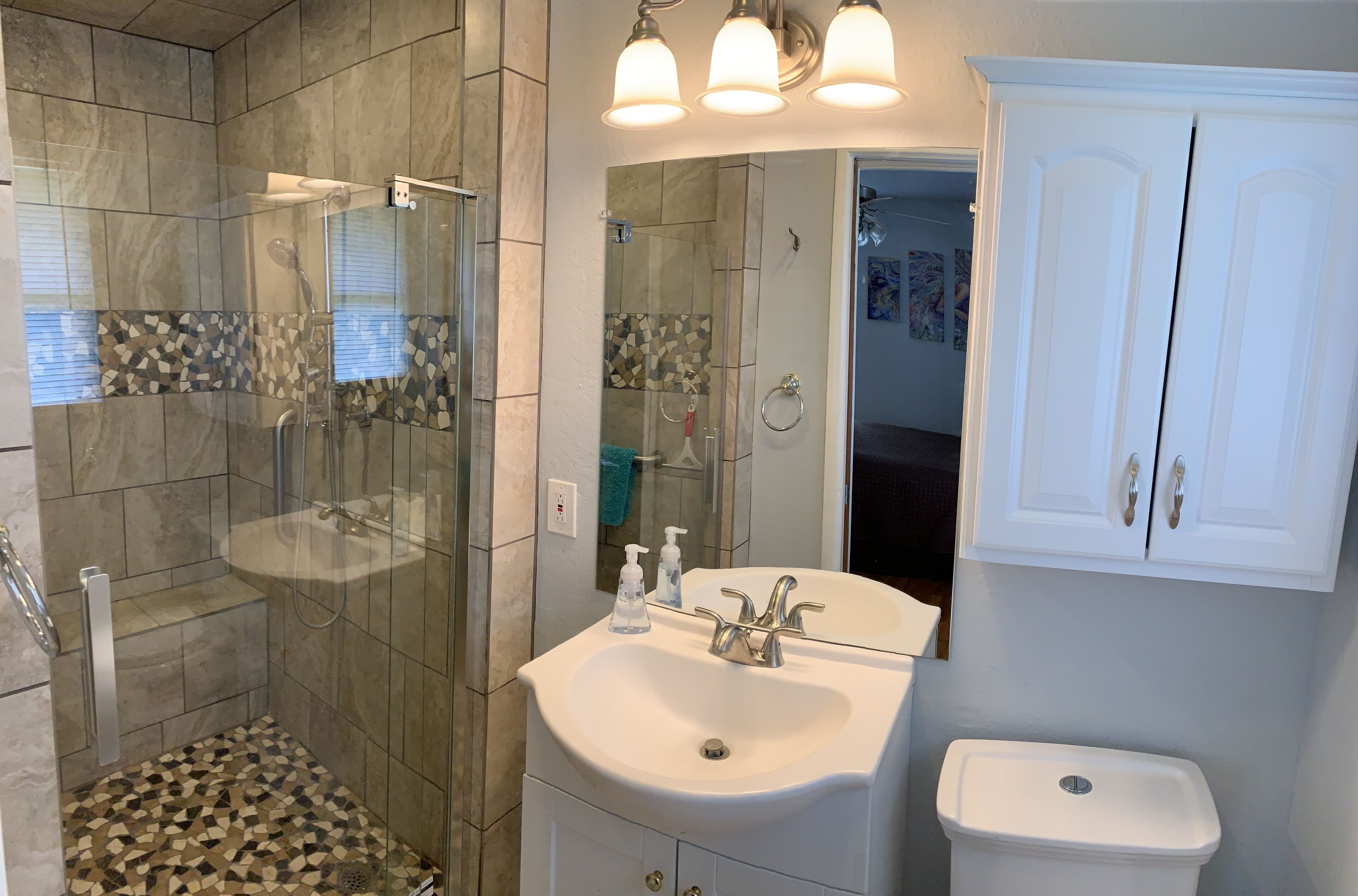 A bathroom with a glass-enclosed shower, a white sink with a mirror, and a white toilet.