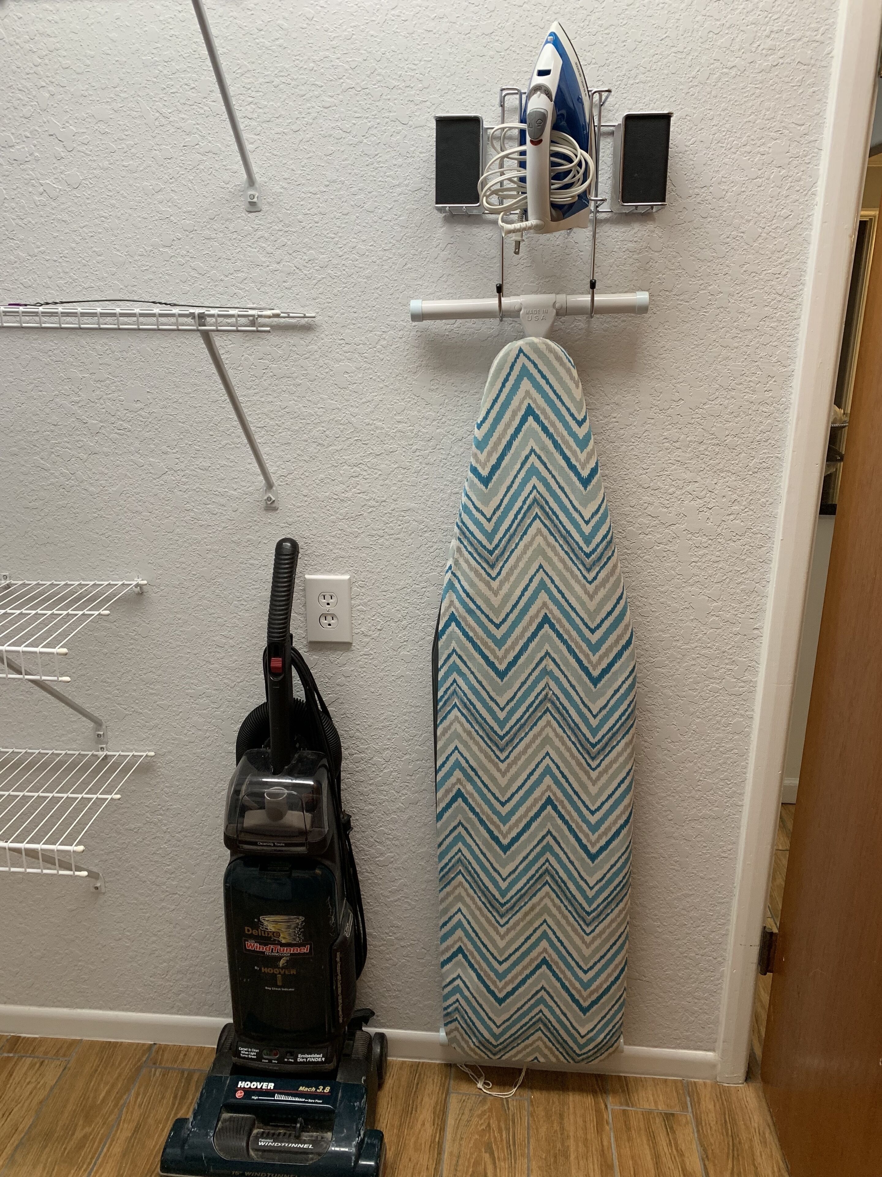 Una habitación con un aspirador, una tabla de planchar y una regleta eléctrica en la pared.