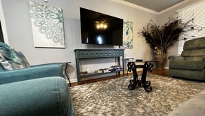 A living room with a flat-screen TV, a console table, and two armchairs.
