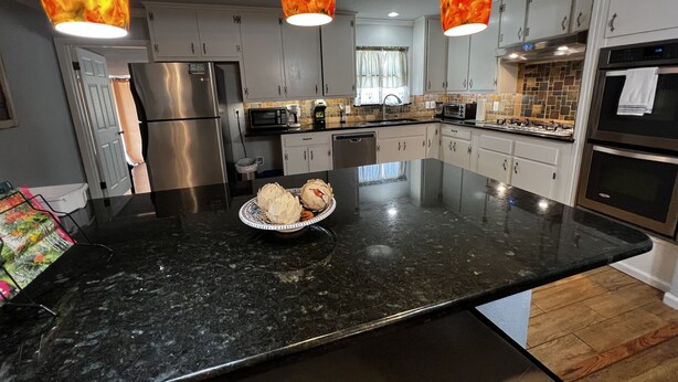 A modern kitchen with granite countertops, stainless steel appliances, and pendant lighting.