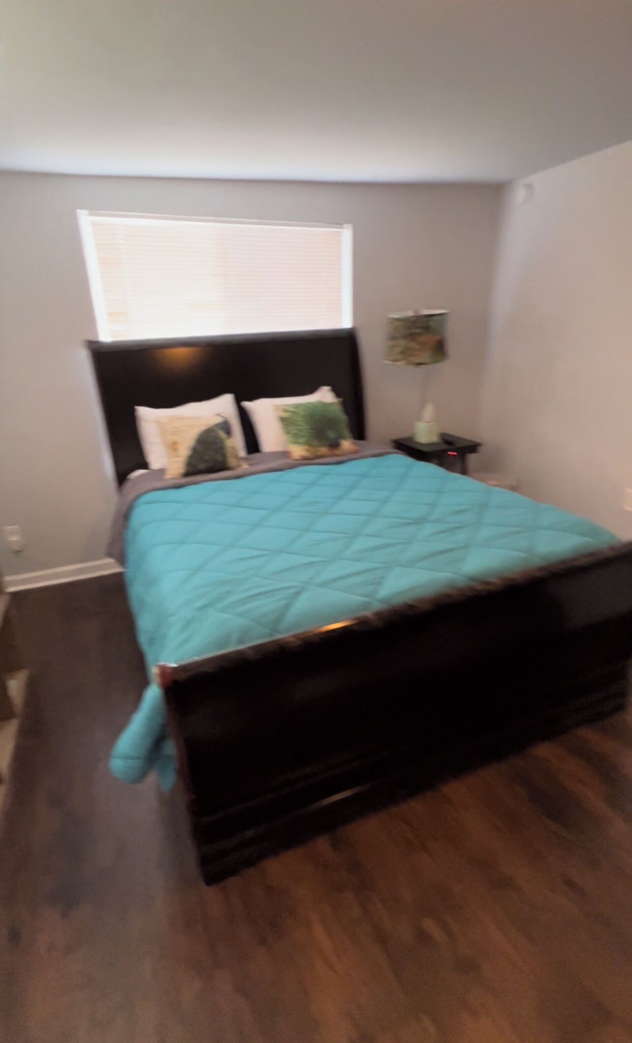 A bedroom with a dark wooden bed, a teal bedspread, and a window with blinds.