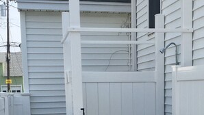 A white outdoor shower area with a wooden platform and a metal faucet. - Great Location / Walk to Everything!  4BR Big Backyard (Beach Haven)