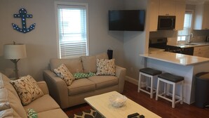 A living room with a sofa, a coffee table, and a TV. There's a kitchen area with a microwave and a sink. - Great Location / Walk to Everything!  4BR Big Backyard (Beach Haven)