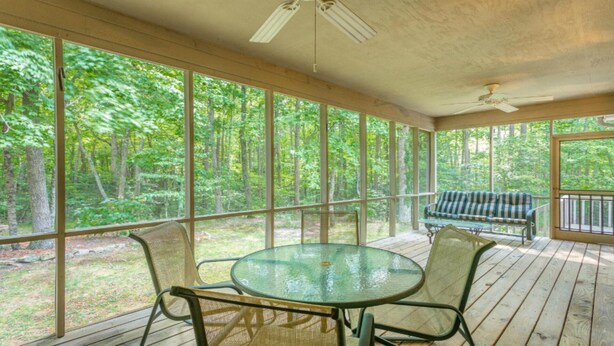 Un espace extérieur abrité, doté d’une table ronde en verre et de chaises, d’un banc, et offrant une vue sur une forêt grâce à de grandes fenêtres.