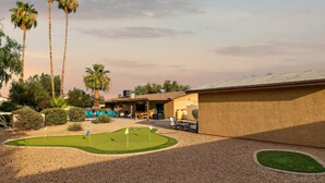 A golf course with a putting green, a patio area with outdoor seating, and palm trees. - Private Resort on 3/4 Acre Game Room Putting Green (Phoenix)