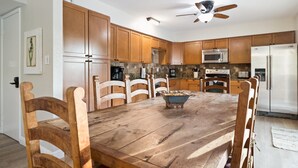 A kitchen with wooden cabinets, a dining table, chairs, a ceiling fan, a microwave, a refrigerator, and a coffee maker. - Private Resort on 3/4 Acre Game Room Putting Green (Phoenix)