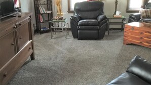 A living room with a leather sofa, a wooden cabinet, a bookshelf, a lamp, and a clock on the wall. - Main Floor 2 bedroom, 1 bath, Easy Walk to Mayo Clinic, trails, parks, shopping (Rochester)