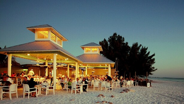 Een restaurant aan het strand met terras en een overdekt gedeelte, met uitzicht op de oceaan.
