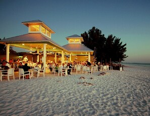 En restaurang vid stranden med uteservering och ett takförsett område, med utsikt över havet.