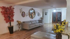 Een ruime woonkamer met een grijze bank, houten vloeren en decoratieve muurkunst.