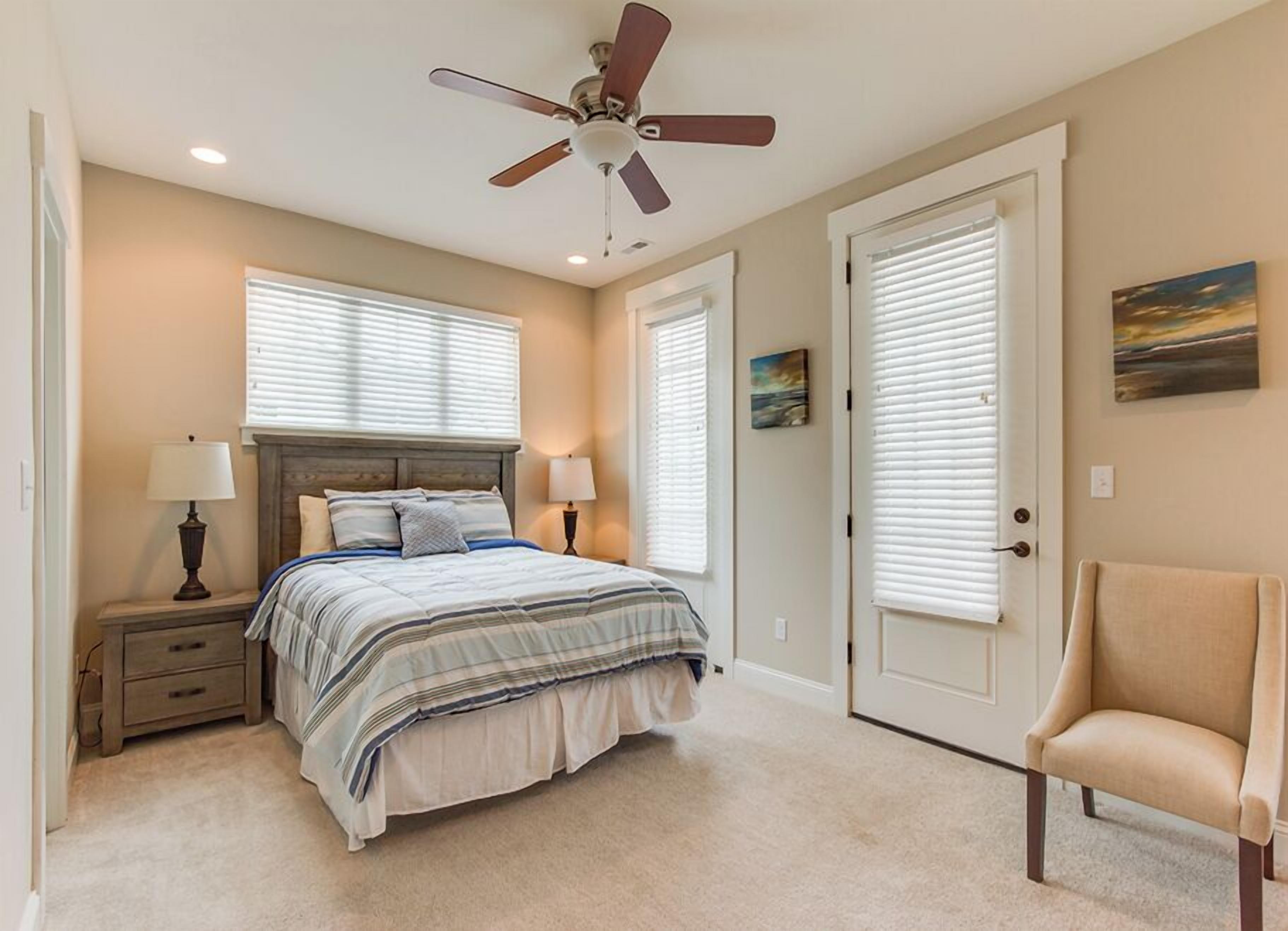 A bedroom with a bed, bedside lamps, a ceiling fan, and a chair.