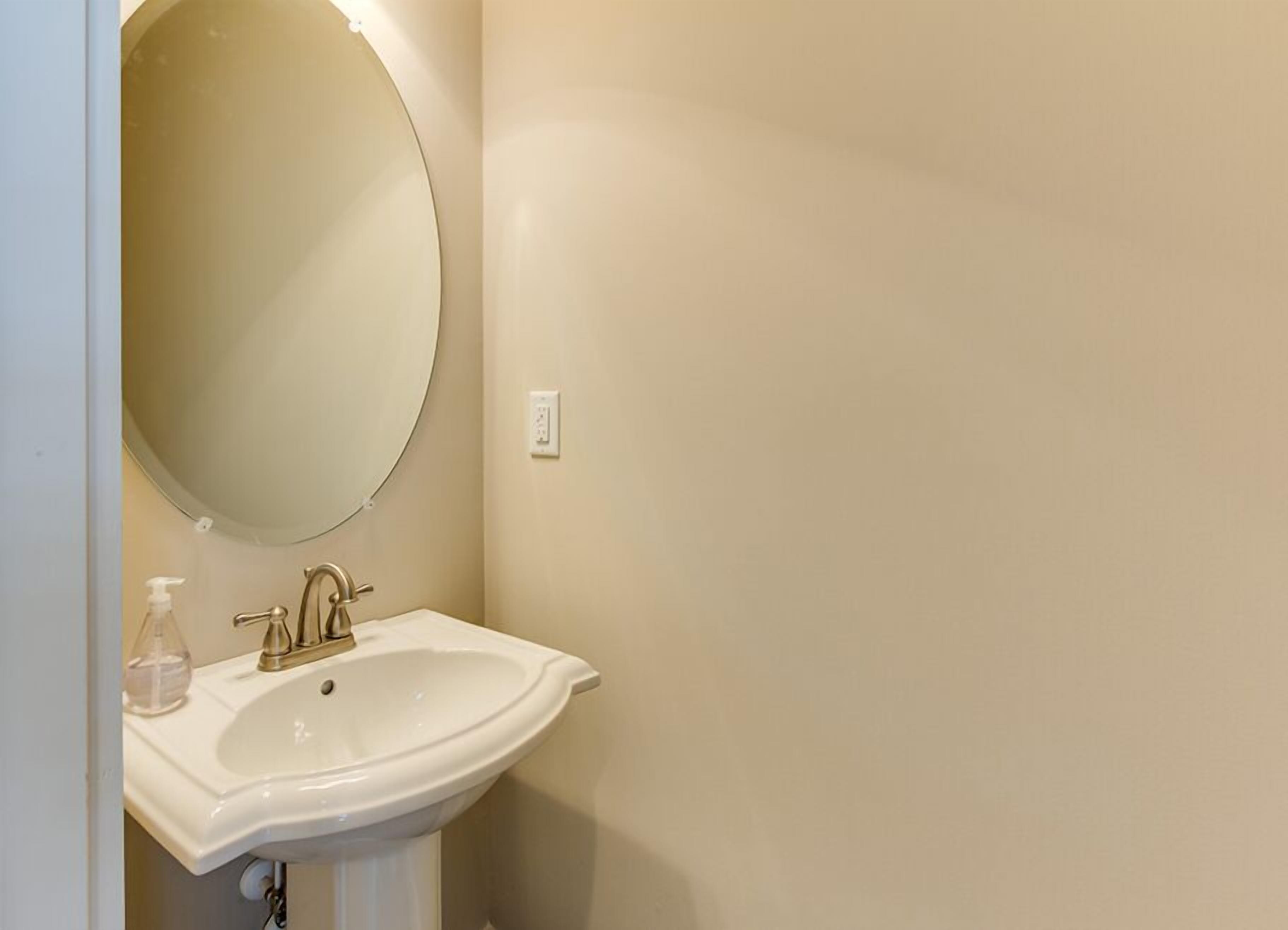 A bathroom with a white sink, a round mirror, and a soap dispenser.