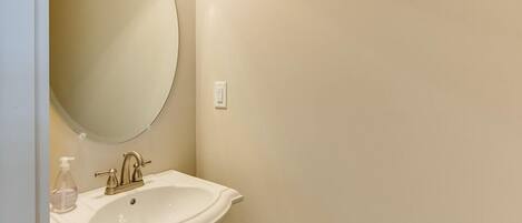 A bathroom with a white sink, a round mirror, and a soap dispenser.
