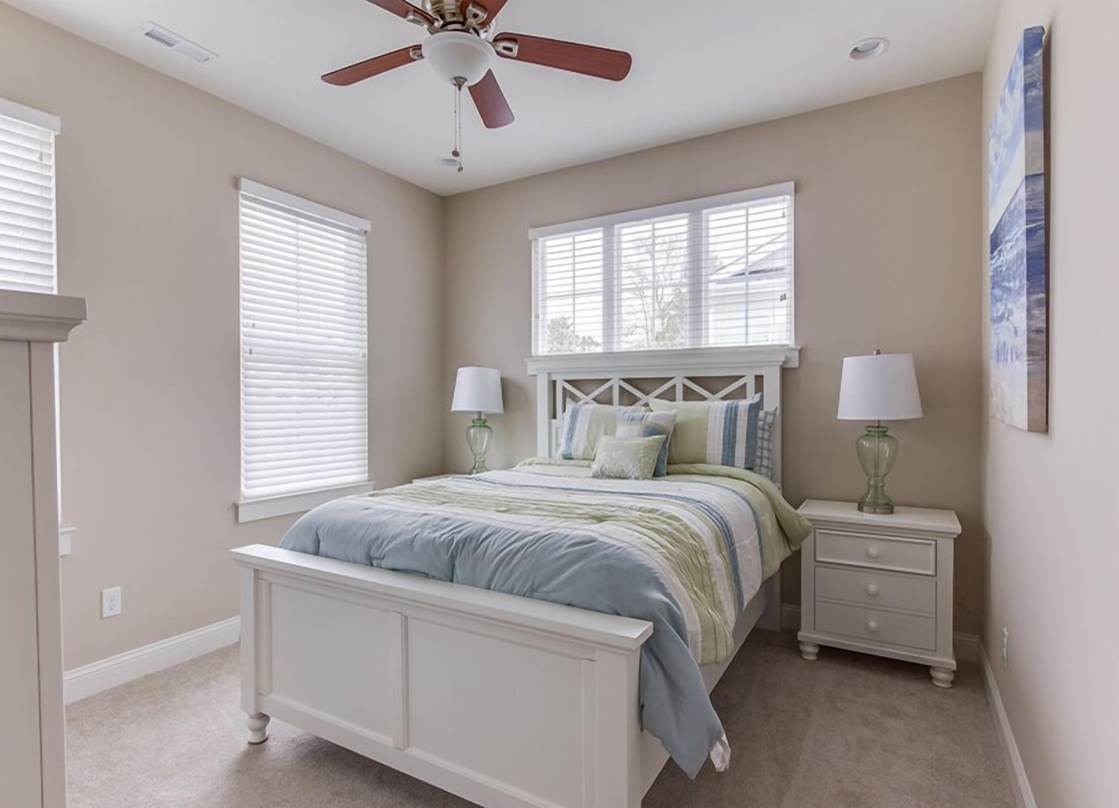 A bedroom with a bed, two bedside tables, a ceiling fan, and windows.