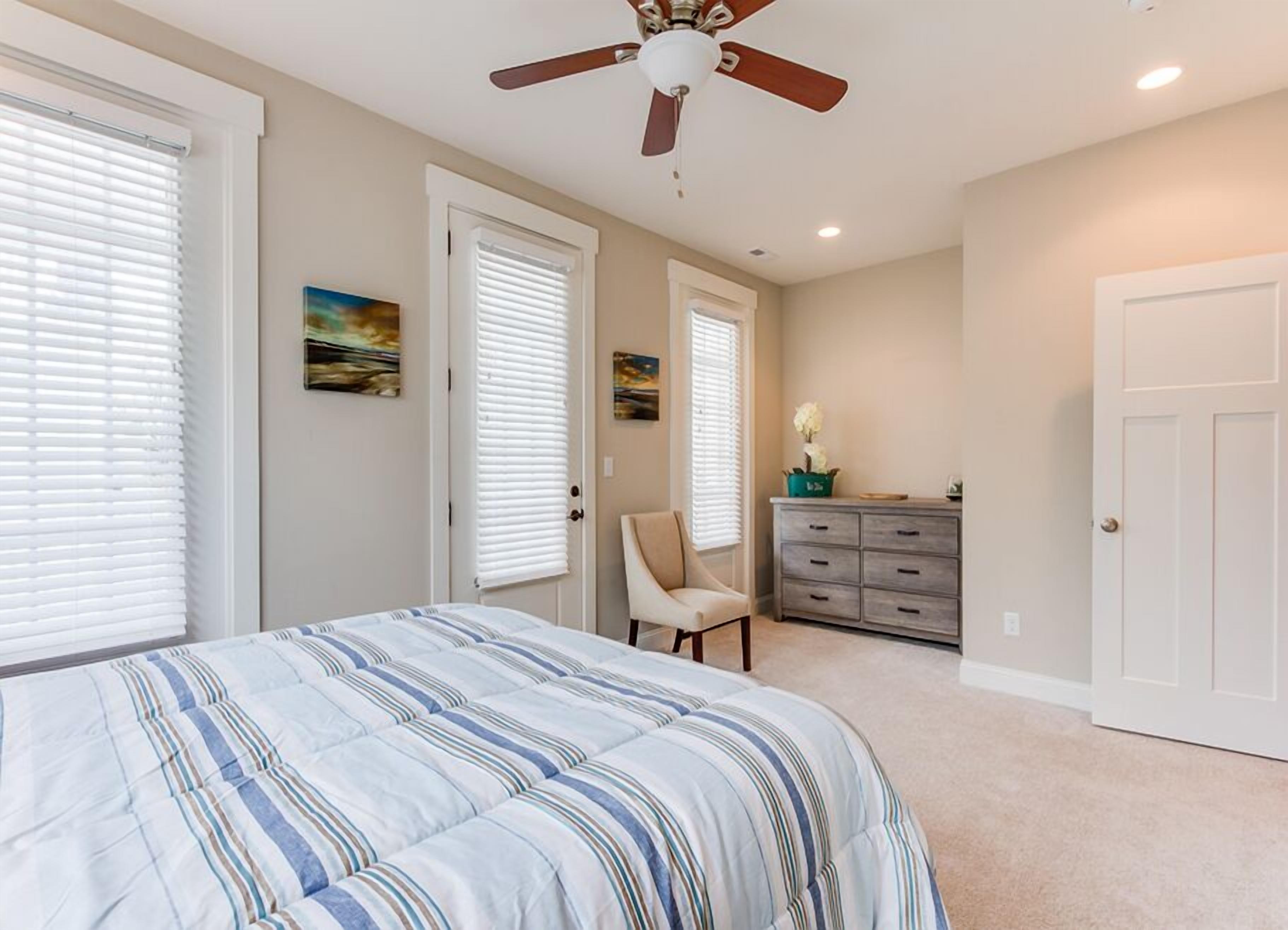 Une chambre à coucher comprenant un lit, un ventilateur de plafond, une commode et deux portes.